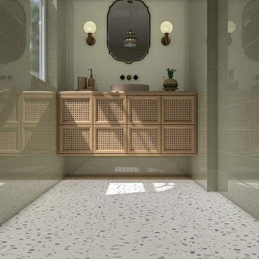 Contemporary bathroom featuring Veneto Medium White 60cm x 60cm terrazzo effect porcelain floor tiles, paired with pale green wall tiles, a wooden cane vanity and brass details.