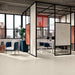 Modern commercial interior featuring Veneto Micro Sand concrete effect porcelain floor tiles, creating a bright, minimalist workspace with black-framed glass partitions, terrazzo effect feature panels, blue upholstered seating and warm contemporary accents.