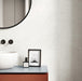 Contemporary bathroom featuring Veneto Micro White concrete effect porcelain wall tiles, styled with a minimalist vanity, black wall-mounted taps, a round mirror and warm modern accents for a clean, elegant interior.