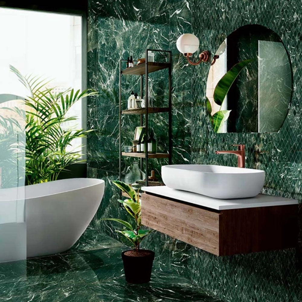 Bathroom interior featuring Grand Verde Alpi Polished Marble effect 60 × 120cm porcelain wall and floor tiles, showcasing deep green tones with striking white veining, paired with a floating wooden vanity, freestanding bath, and brushed brass fittings for a bold, luxurious finish.