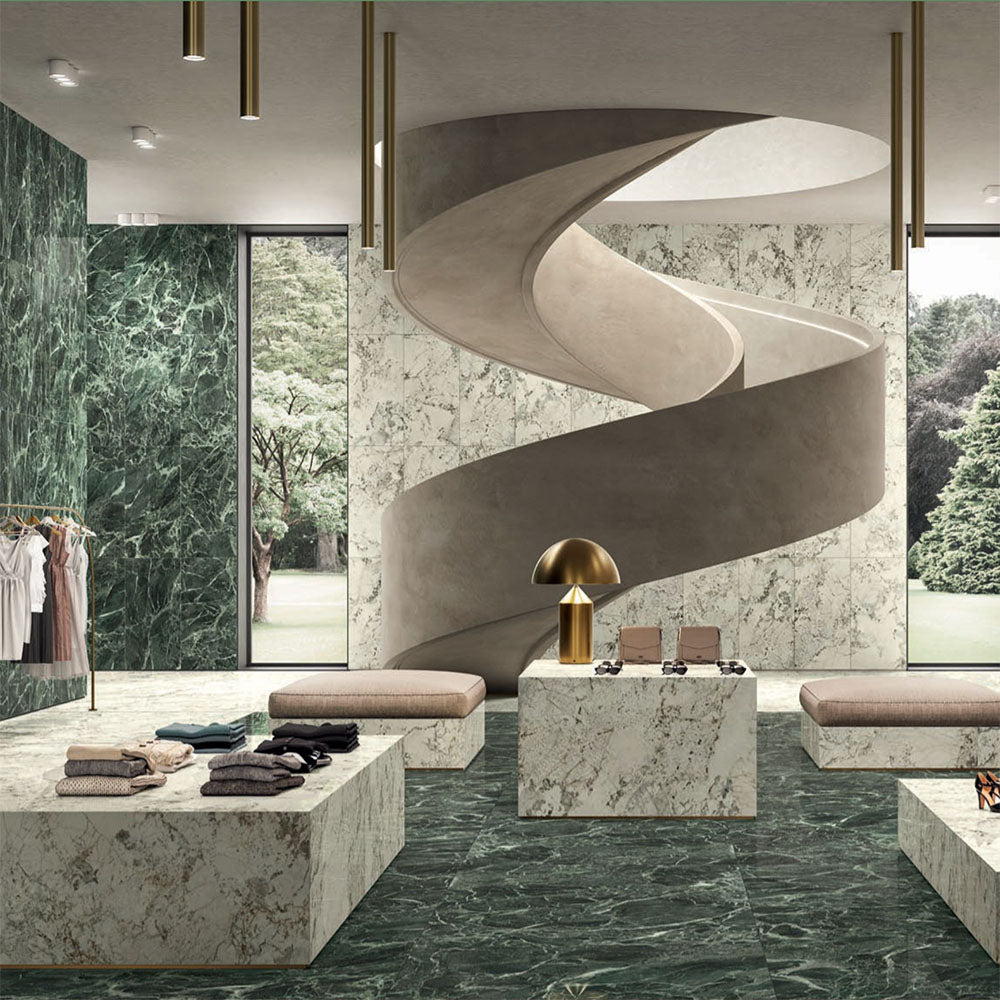 Retail interior featuring Grand Verde Apia Polished Green Marble effect 60 × 60cm porcelain wall and floor tiles, styled with sculptural staircase, stone display plinths, and rich green tones with striking natural veining.