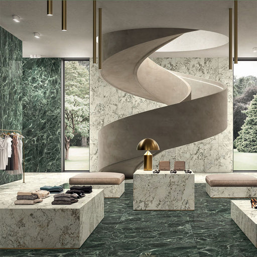 Retail interior featuring Grand Verde Apia Polished Green Marble effect 60 × 60cm porcelain wall and floor tiles, styled with sculptural staircase, stone display plinths, and rich green tones with striking natural veining.