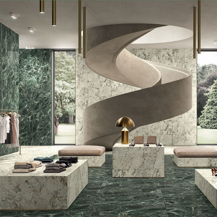 Retail interior featuring Grand Verde Apia Polished Green Marble effect 60 × 60cm porcelain wall and floor tiles, styled with sculptural staircase, stone display plinths, and rich green tones with striking natural veining.