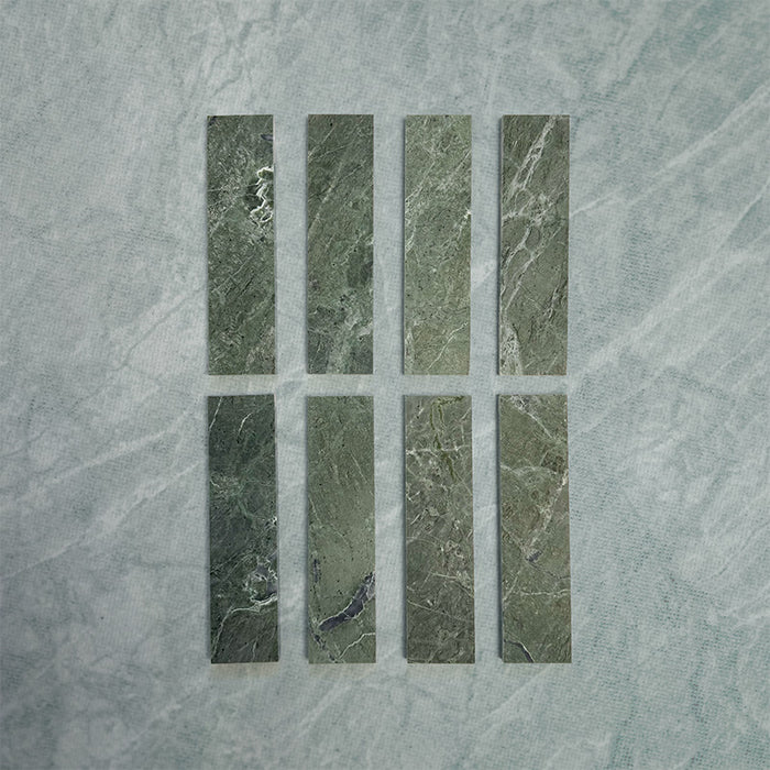 Eight Fitzrovia Verde 5 x 20cm honed natural marble tiles arranged on a soft neutral backdrop, showcasing rich green tones with subtle natural veining and variation, highlighting the depth and character of the stone.
