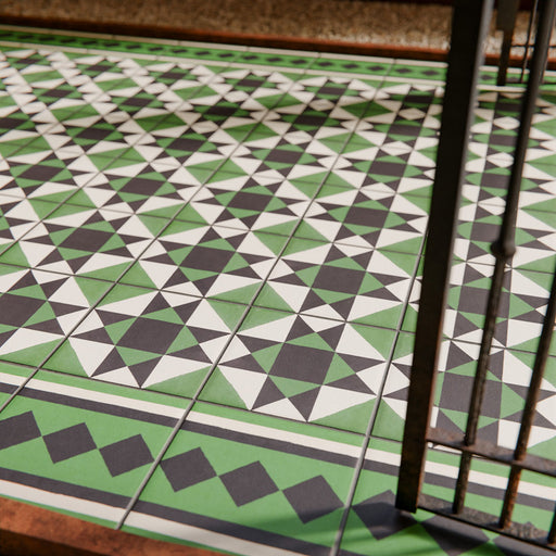Maison Green Victorian Side/Border 20cm x 20cm, Victorian border floor tile shown in walkway setting, geometric diamond border pattern, green, black and white colour palette, matt finish, classic heritage Victorian design.