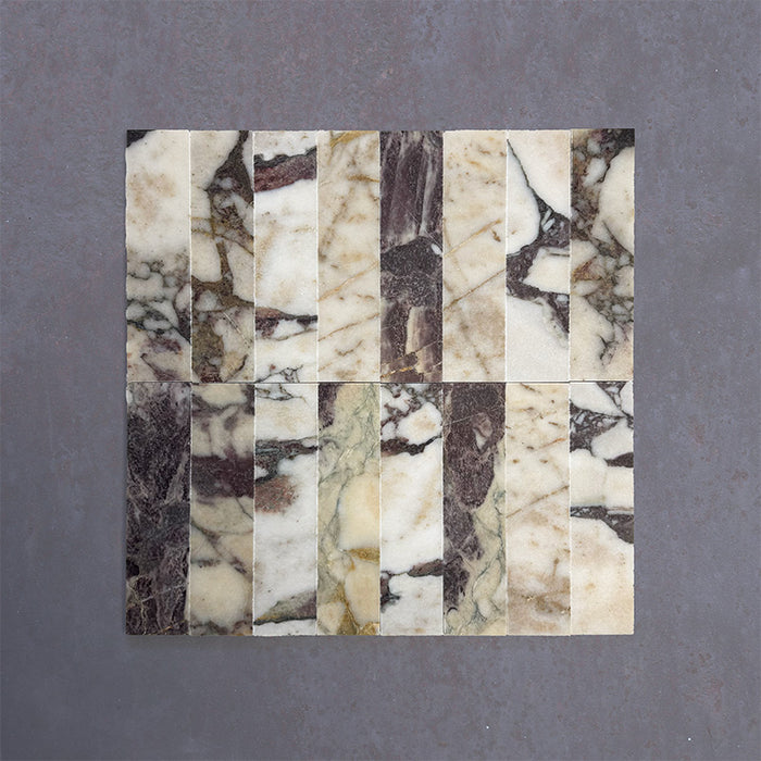 Group of Fitzrovia Viola 5x20cm honed natural marble brick tiles arranged in a neat layout, showcasing a white base with varied burgundy, gold, and grey veining, and a smooth, refined finish.