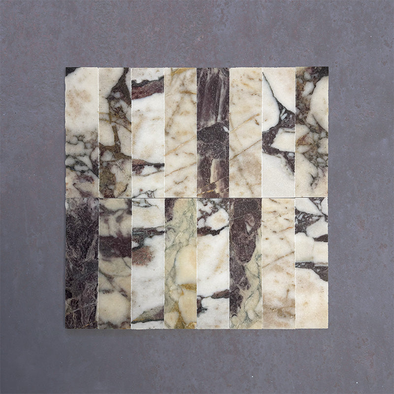 Group of Fitzrovia Viola 5x20cm honed natural marble brick tiles arranged in a neat layout, showcasing a white base with varied burgundy, gold, and grey veining, and a smooth, refined finish.