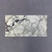 Fitzrovia Viola 30.5x61cm natural marble tiles with a honed finish, featuring a white base with striking green and burgundy veining, shown as a single tile sample laid horizontally against a dark textured backdrop.