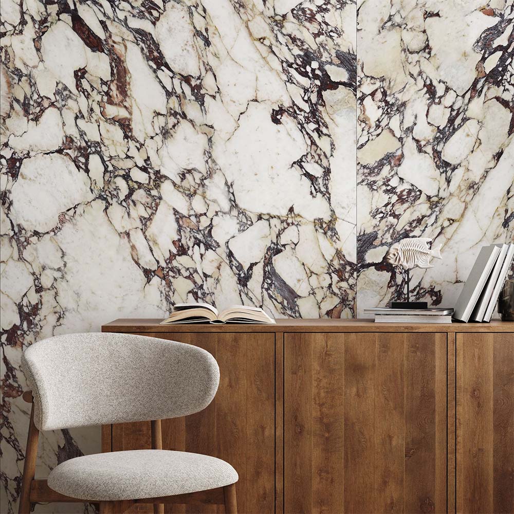 Interior setting featuring Grand Violetta Polished Marble effect 60 × 120cm porcelain wall tiles, showcasing a creamy base with dramatic burgundy and charcoal veining, styled behind a wooden sideboard with decorative objects for a bold, statement finish.