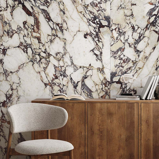 Interior setting featuring Grand Violetta Polished Marble effect 60 × 120cm porcelain wall tiles, showcasing a creamy base with dramatic burgundy and charcoal veining, styled behind a wooden sideboard with decorative objects for a bold, statement finish.