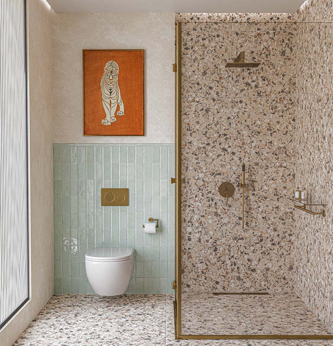 Vito Dolomite 60cm x 60cm terrazzo effect tiles with a 4D brushed finish, featuring a detailed mix of cream, beige, grey and warm earthy fragments across the bathroom floor and shower walls, paired with soft mint green tiles and brushed brass fittings.