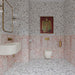 Vito Moonstone 60cm x 60cm terrazzo effect tiles, featuring a speckled mix of soft grey, charcoal and warm earthy tones across the bathroom floor and walls, paired with pink marble effect tiles and brass details.