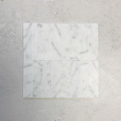 Group of Fitzrovia White 5x20cm honed natural marble brick tiles arranged in a neat layout, showcasing soft white tones, subtle grey veining, and a smooth, refined finish ideal for wall installations.