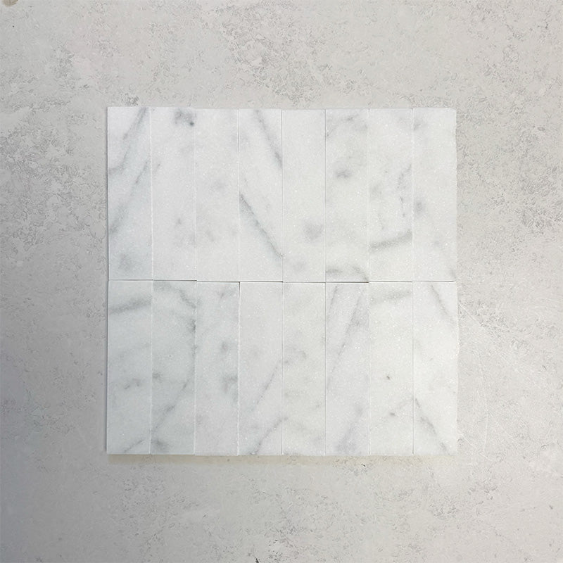 Group of Fitzrovia White 5x20cm honed natural marble brick tiles arranged in a neat layout, showcasing soft white tones, subtle grey veining, and a smooth, refined finish ideal for wall installations.