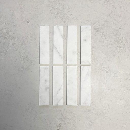 Group of Fitzrovia White 5x20cm honed natural marble brick tiles arranged in a neat layout, showcasing soft white tones, subtle grey veining, and a smooth, refined finish ideal for wall installations.