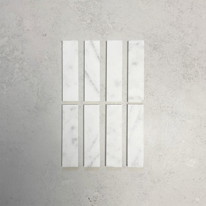 Group of Fitzrovia White 5x20cm honed natural marble brick tiles arranged in a neat layout, showcasing soft white tones, subtle grey veining, and a smooth, refined finish ideal for wall installations.