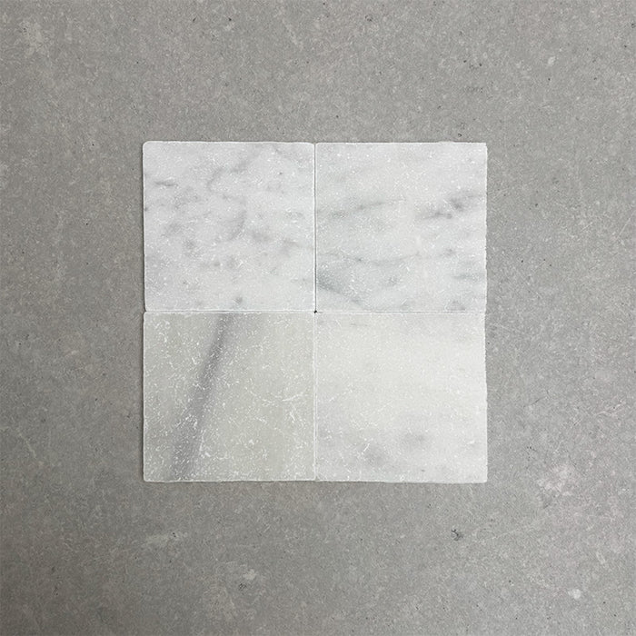 Fitzrovia White 15.2x15.2cm tumbled natural marble tiles arranged in a square layout, showcasing soft white tones, subtle grey veining, tonal variation, and an aged, lightly textured finish.