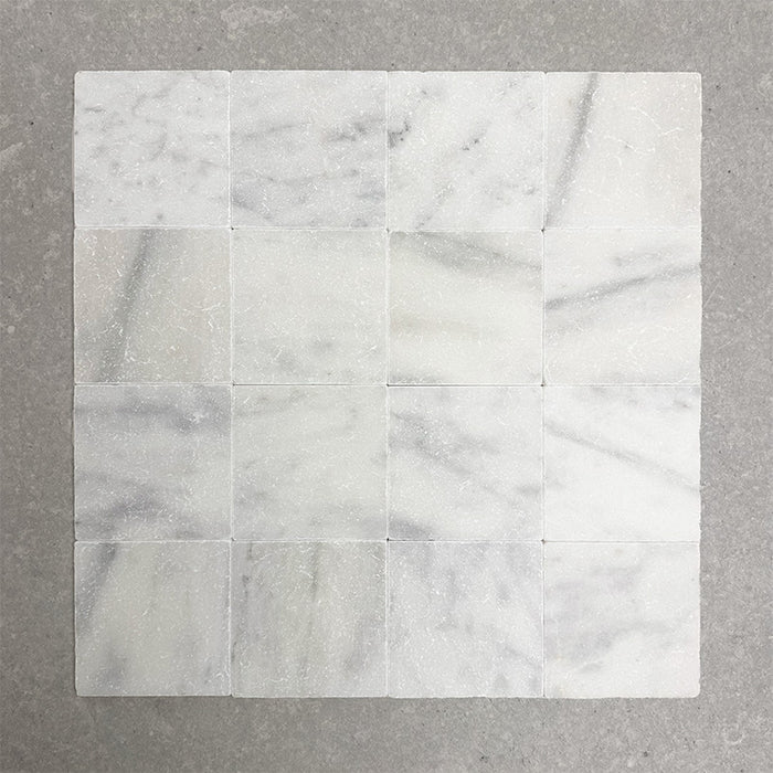 Group of Fitzrovia White 15.2x15.2cm tumbled natural marble tiles arranged in a square layout, showcasing soft white tones, subtle grey veining, tonal variation, and an aged, lightly textured finish.