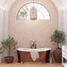 Bathroom featuring Zeina Moroccan Cotto White ceramic wall tiles in a repeating Moroccan style geometric pattern, paired with a freestanding copper bath, terracotta effect floor tiles, arched window, woven pendant light and olive trees for a warm Mediterranean-inspired retreat.