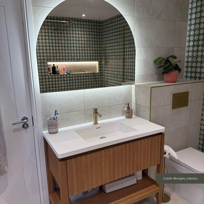 Contemporary bathroom featuring Zeina Moroccan Emerald Green ceramic wall tiles in a Moroccan style geometric pattern within the shower enclosure, paired with large-format stone effect wall tiles, a floating oak vanity, brushed brass fittings and an illuminated arched mirror.