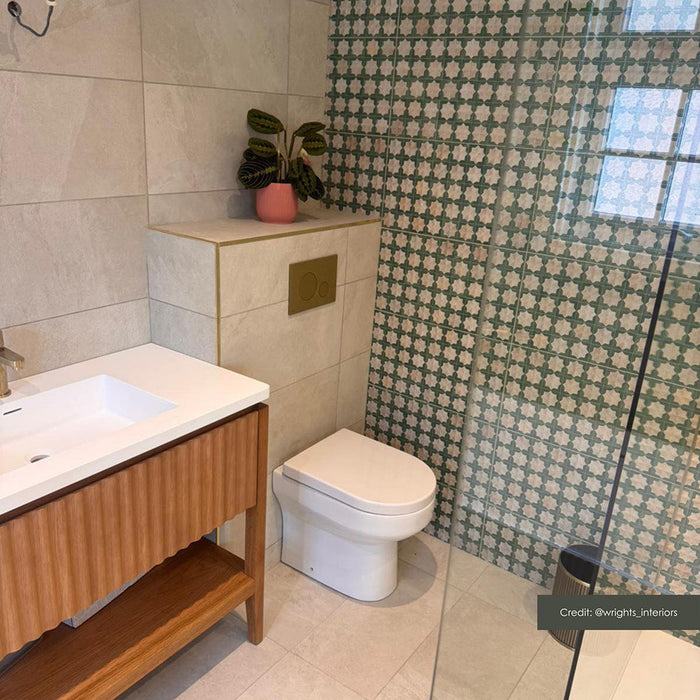 Contemporary bathroom featuring Zeina Moroccan Emerald Green ceramic wall tiles in a Moroccan style geometric pattern within the shower enclosure, paired with large-format stone effect wall tiles, a floating oak vanity, brushed brass fittings and an illuminated arched mirror.
