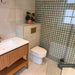 Contemporary bathroom featuring Zeina Moroccan Emerald Green ceramic wall tiles in a Moroccan style geometric pattern within the shower enclosure, paired with large-format stone effect wall tiles, a floating oak vanity, brushed brass fittings and an illuminated arched mirror.
