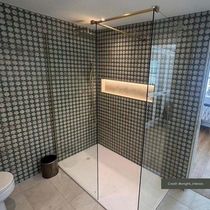 Contemporary bathroom featuring Zeina Moroccan Emerald Green ceramic wall tiles in a Moroccan style geometric pattern within the shower enclosure, paired with large-format stone effect wall tiles, a floating oak vanity, brushed brass fittings and an illuminated arched mirror.