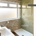 Bathroom featuring Zellij Bone Brick 6.5x20cm Moroccan-style wall tiles, arranged in a herringbone pattern in soft beige tones, paired with green marble-effect shower tiles, a glass shower screen and brushed brass fixtures.