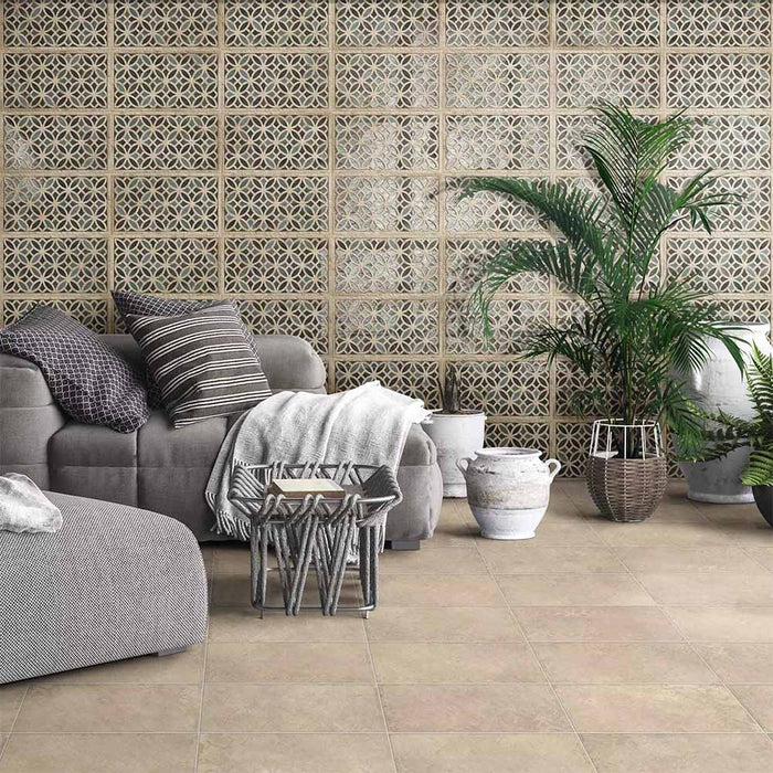 Living room featuring Ziza Emerald Green Moroccan style decorative porcelain wall tiles, showcasing an intricate geometric floral pattern in rich emerald green, charcoal, beige and cream tones with an aged finish, paired with warm stone effect floor tiles, soft grey furnishings, natural textures and lush greenery for a relaxed Moroccan-inspired interior.