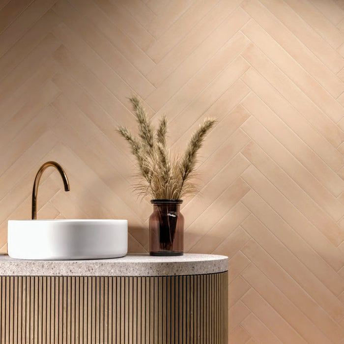 Maldives Clay matt porcelain tiles laid in a herringbone pattern on a bathroom wall, featuring warm clay tones behind a modern basin and brass tap.