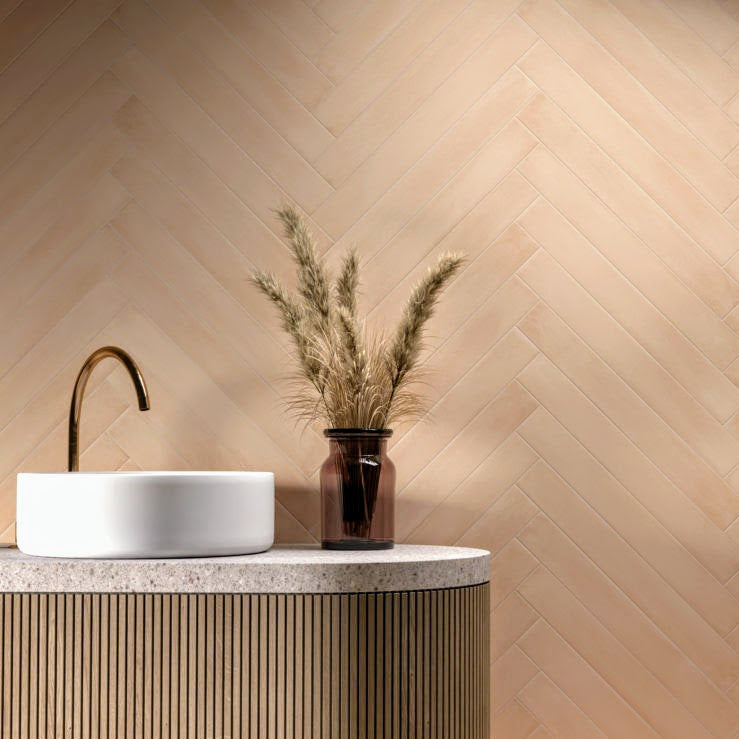 Maldives Clay matt porcelain tiles laid in a herringbone pattern on a bathroom wall, featuring warm clay tones behind a modern basin and brass tap.
