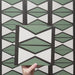 Video showcasing the Geometry Hourglass 20x20cm patterned tile, highlighting its alternating green and cream hourglass design with bold charcoal outlines, and demonstrating how the pattern repeats when multiple tiles are laid together.
