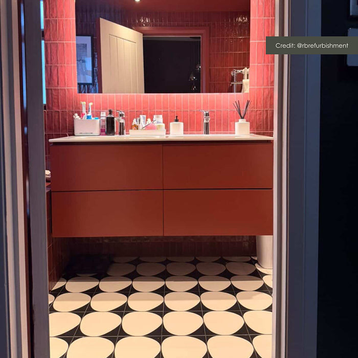 Bathroom interior featuring Pebble Beach Black 20 × 20cm anti-slip porcelain floor tiles, styled in a bold circular pattern with red wall tiles and a floating vanity for a striking, contemporary finish.